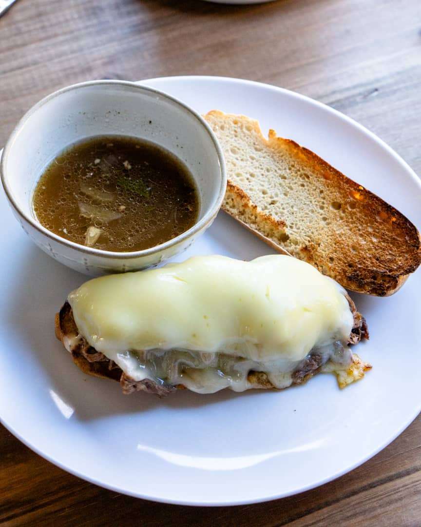 Open faced French dip sandwich with au jus in a bowl next to it.