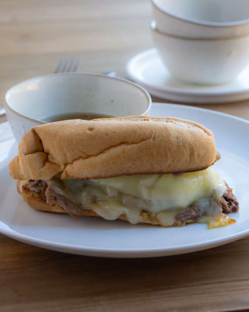 French dip sandwich on a plate with au jus bowl next to it.