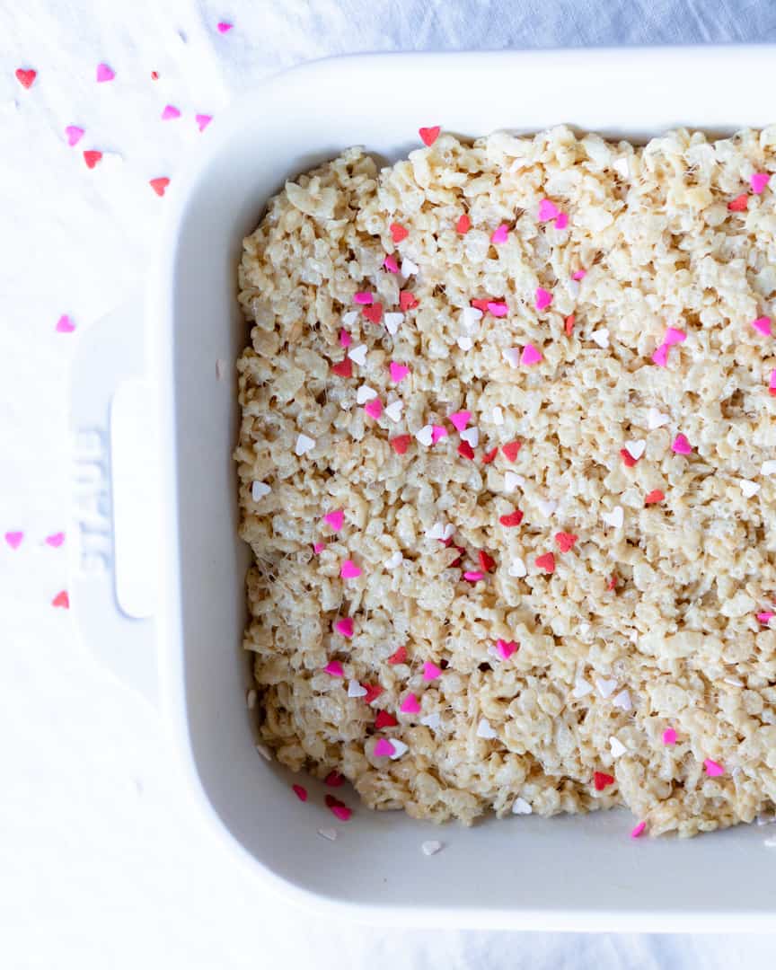 A baking pan with rice krispie treats sprinkled with red, pink, and white hearts.