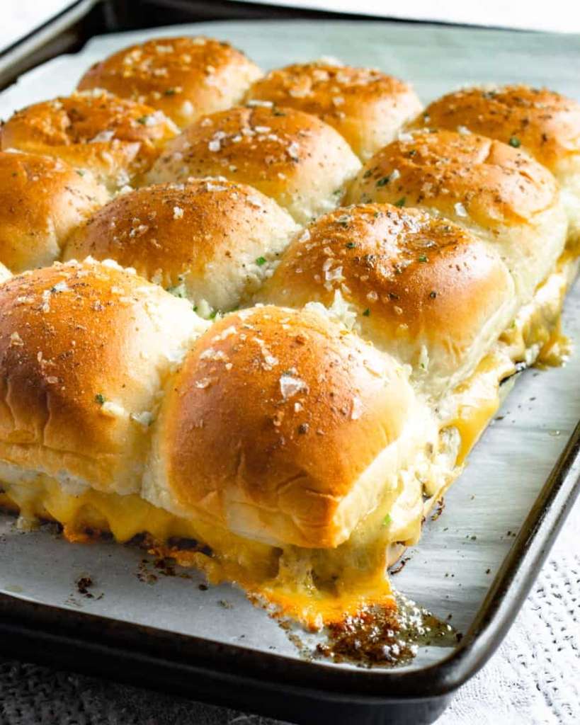 A tray of baked slider buns with melted cheese coming out the sides.