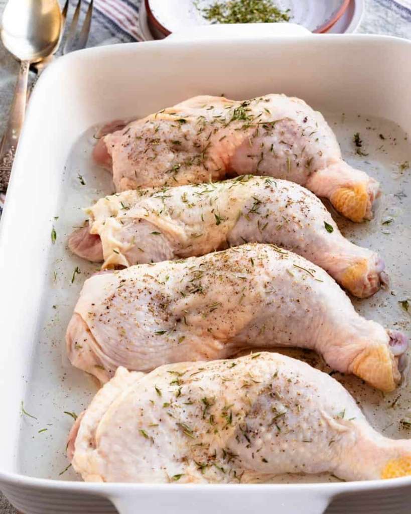 Uncooked chicken legs with herb seasoning on top in baking pan