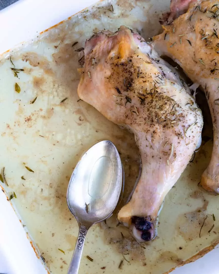 Roated chicken leg in a pan with a spoon sitting in the pan juices.