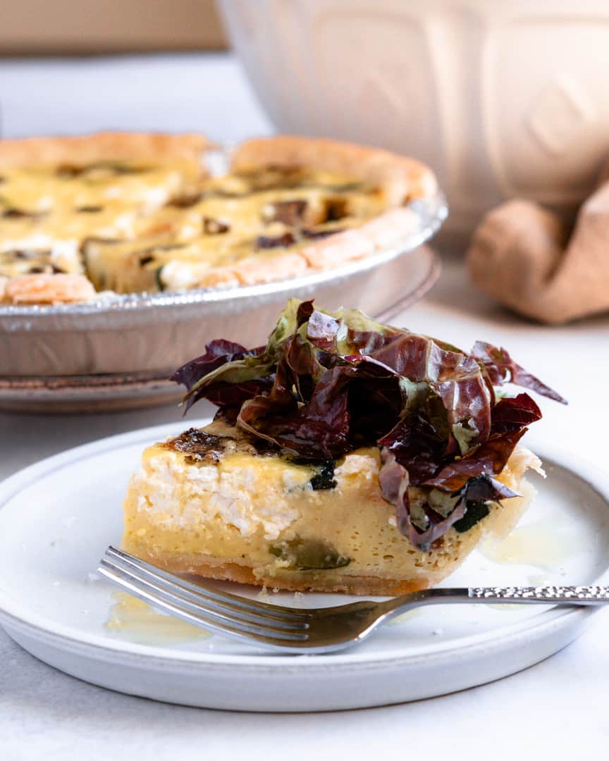 A slice of quiche on a plate with lettuce on top drizzled with olive oil.