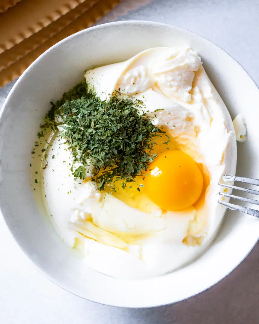 Ricotta cheese with raw egg and dried parsley in a bowl.