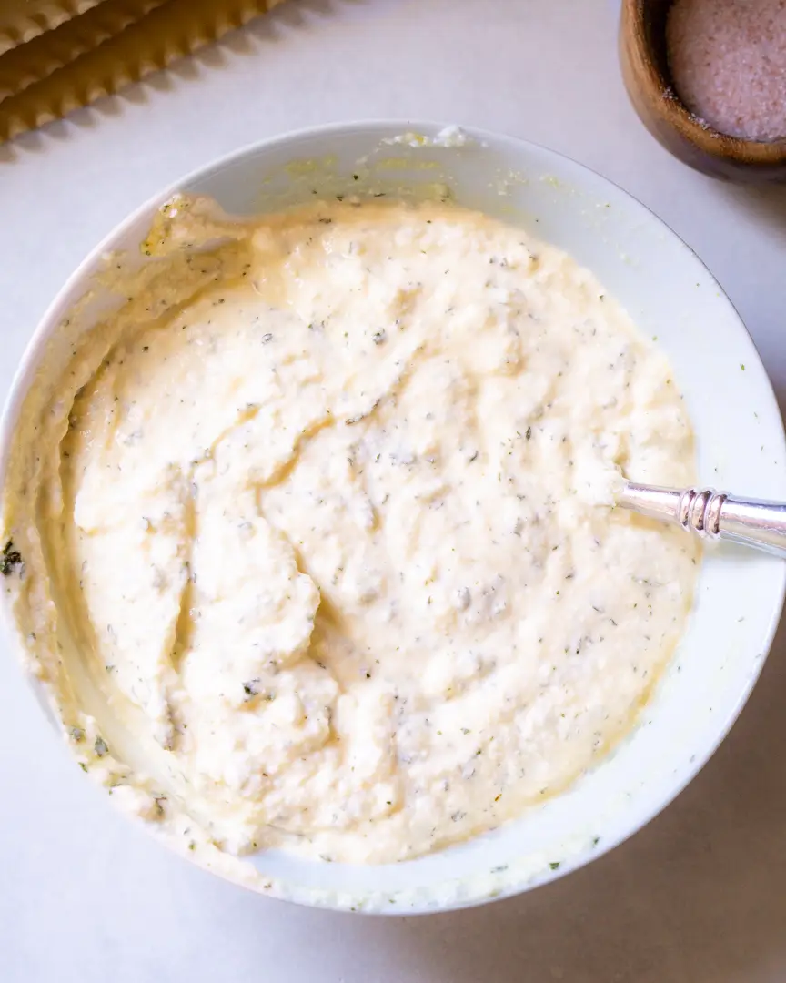 Ricotta cheese in a bowl blended with egg and dried parsley. There is a fork in the bowl