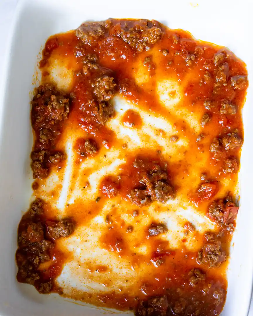 Bottom of a baking pan covered in ground beef with red sauce.