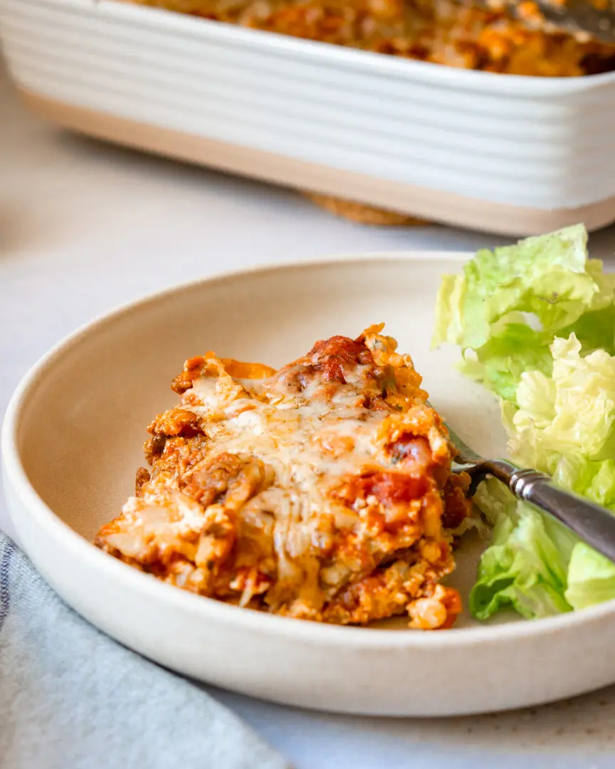 A piece of lasagna on a plate with green salad next to it.