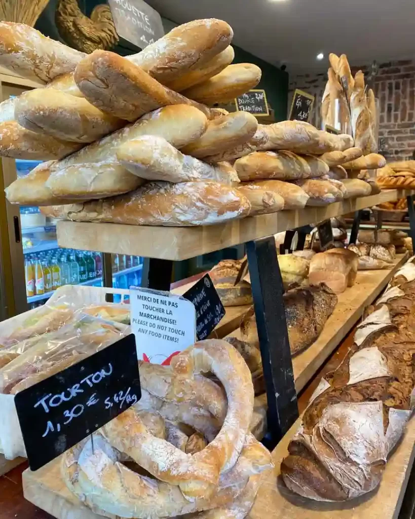 Crusty baguettes and various other baked breads stacked and on display.
