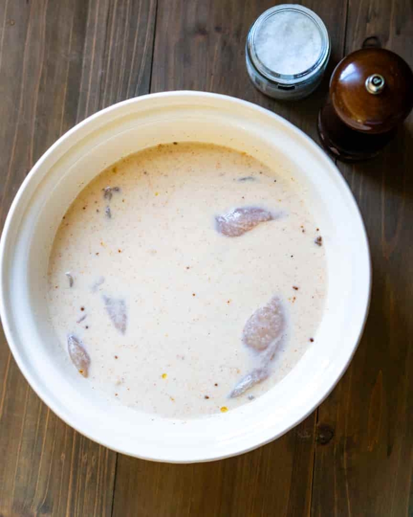 A bowl of buttermilk with chicken tenders marinating in it.