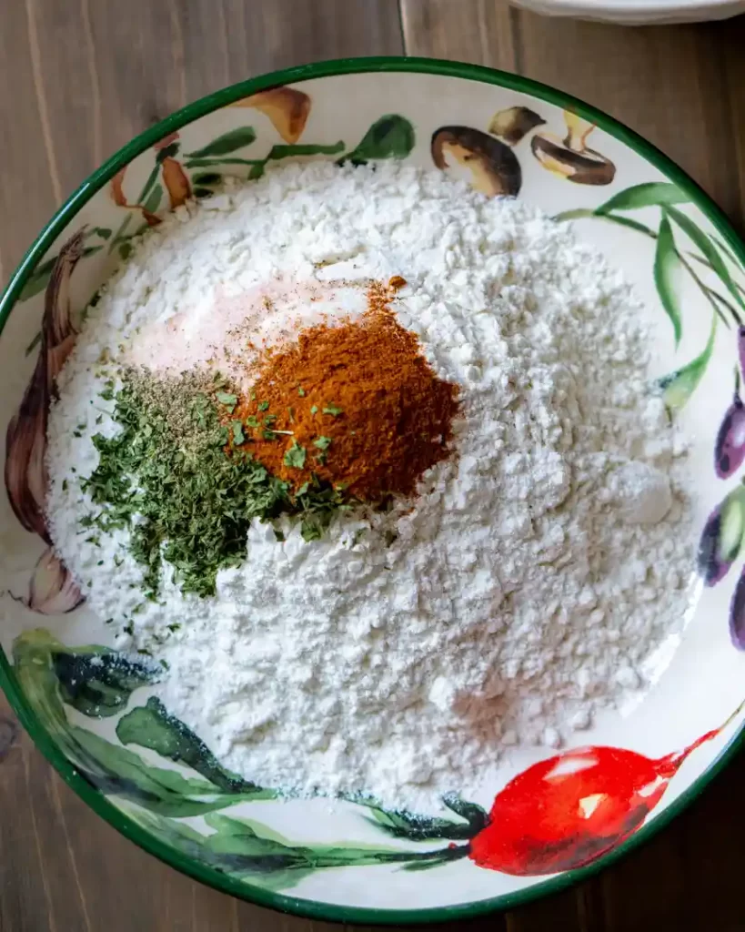 A bowl of flour with herbs and spices on top.