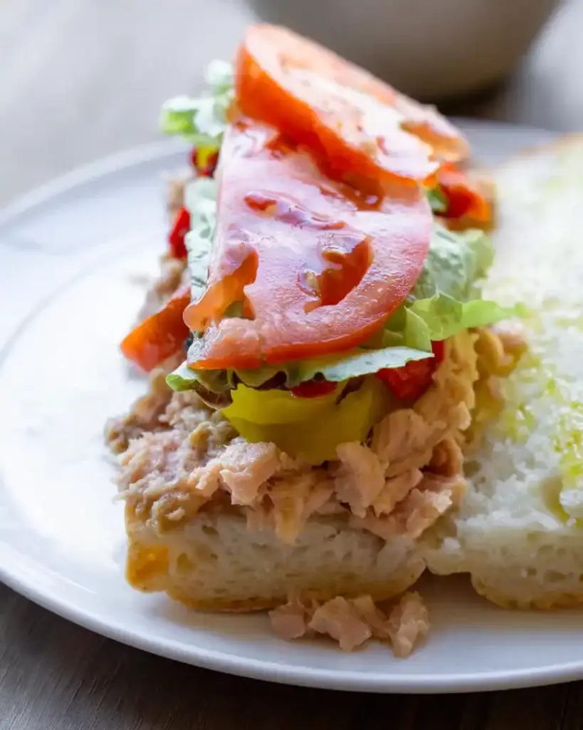 Canned tuna on a open baguette topped with peppers, lettuce, and tomatoes
