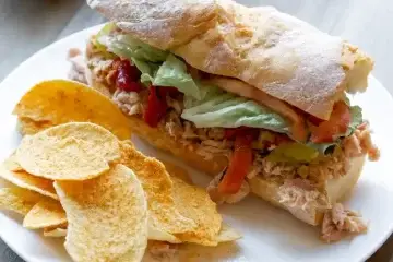 Baguette filled Italian Tuna Sandwich on a plate with chips next to it.
