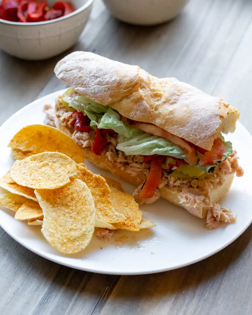 Baguette filled Italian Tuna Sandwich on a plate with chips next to it.
