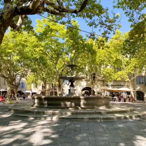 A town square with trees and a large tiered fountain in the middle.