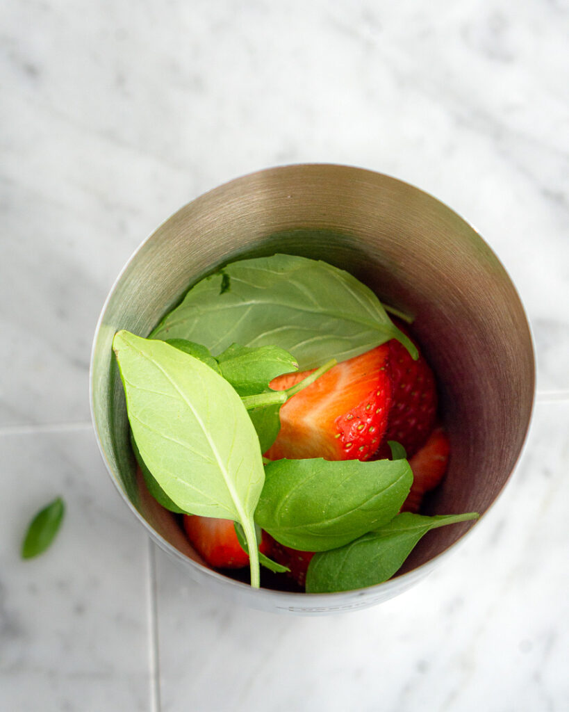 Fresh strawberries and basil leaves in a cocktail shaker.