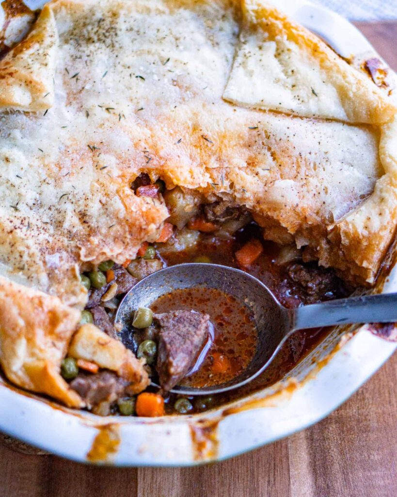 Pot pie with a scoop missing. There is a large spoon ready to scoop more.