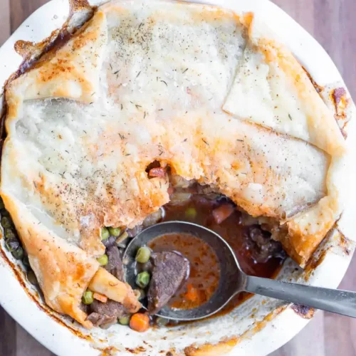 A beef pot pie with a scoop taken out of it. There is a spoon in the scooped out portion of the pie.