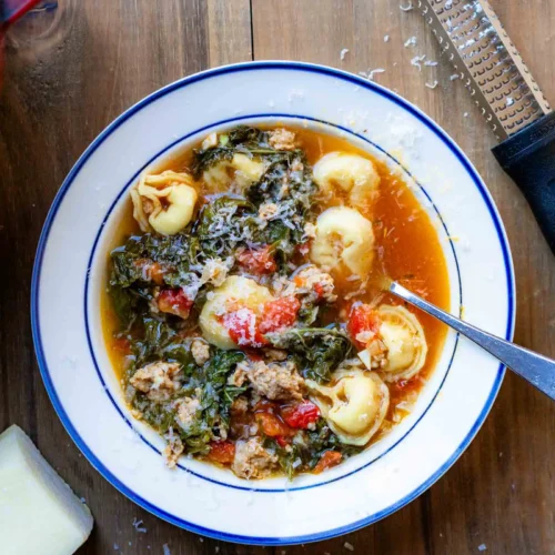 A bowl of tortellini soup with a spoon in it.
