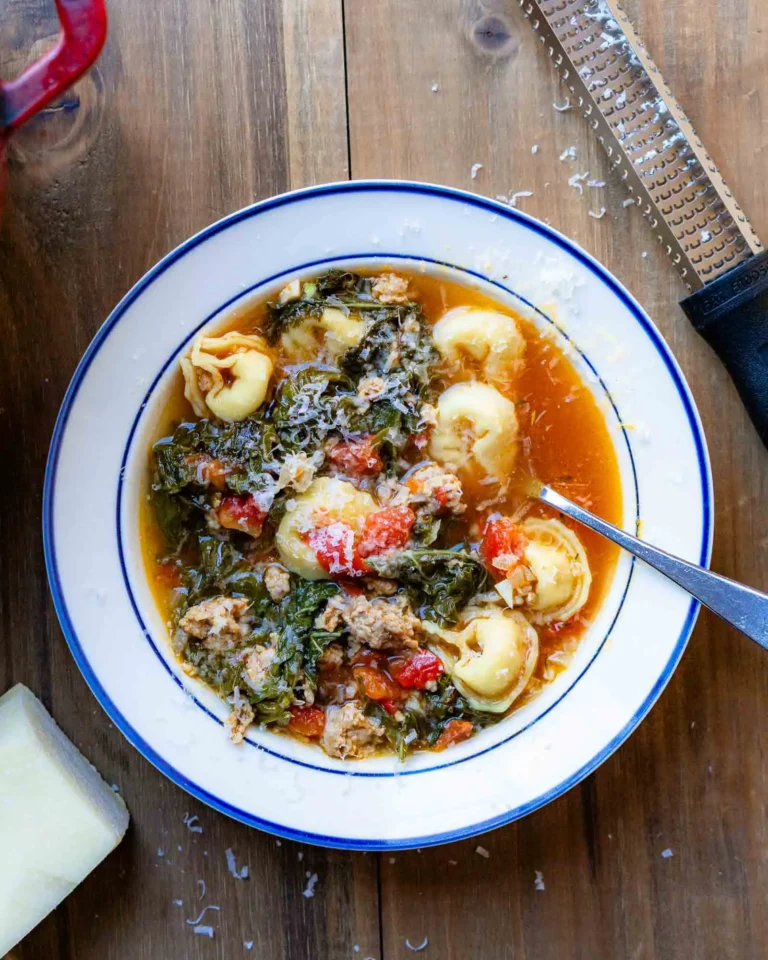 A bowl of tortellini soup with a spoon in it.