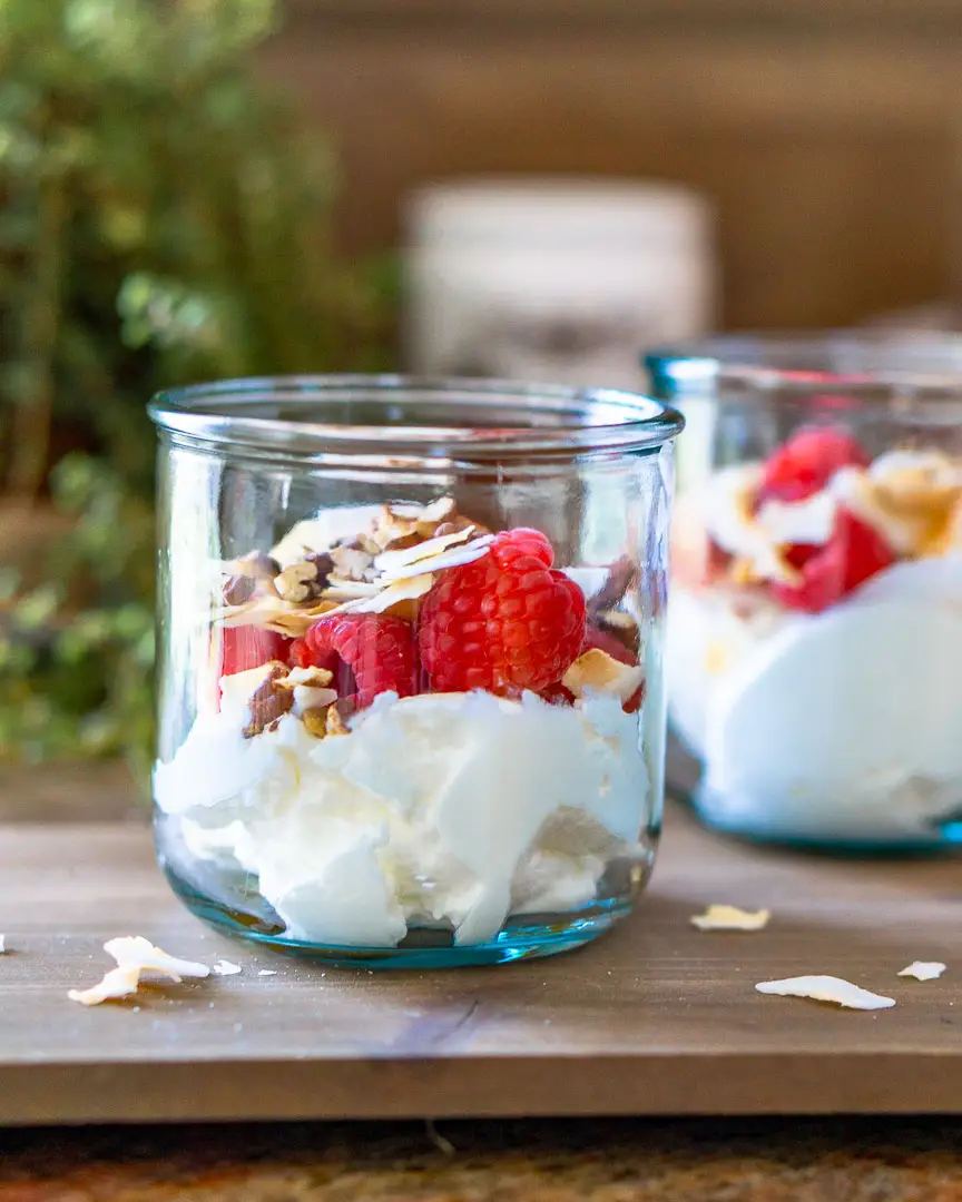 Two glasses of yogurt parfait topped with fruit, nuts, and coconut flakes.
