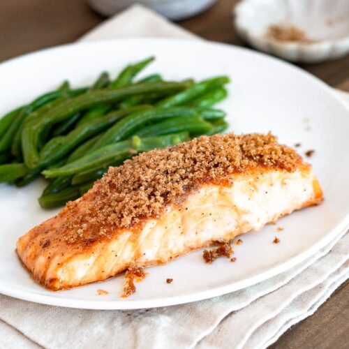 A salmon fillet with brown sugar topping on a plate with green beans.