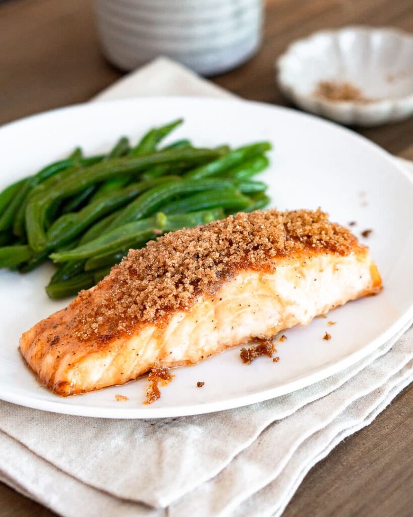 A salmon fillet with brown sugar topping on a plate with green beans.