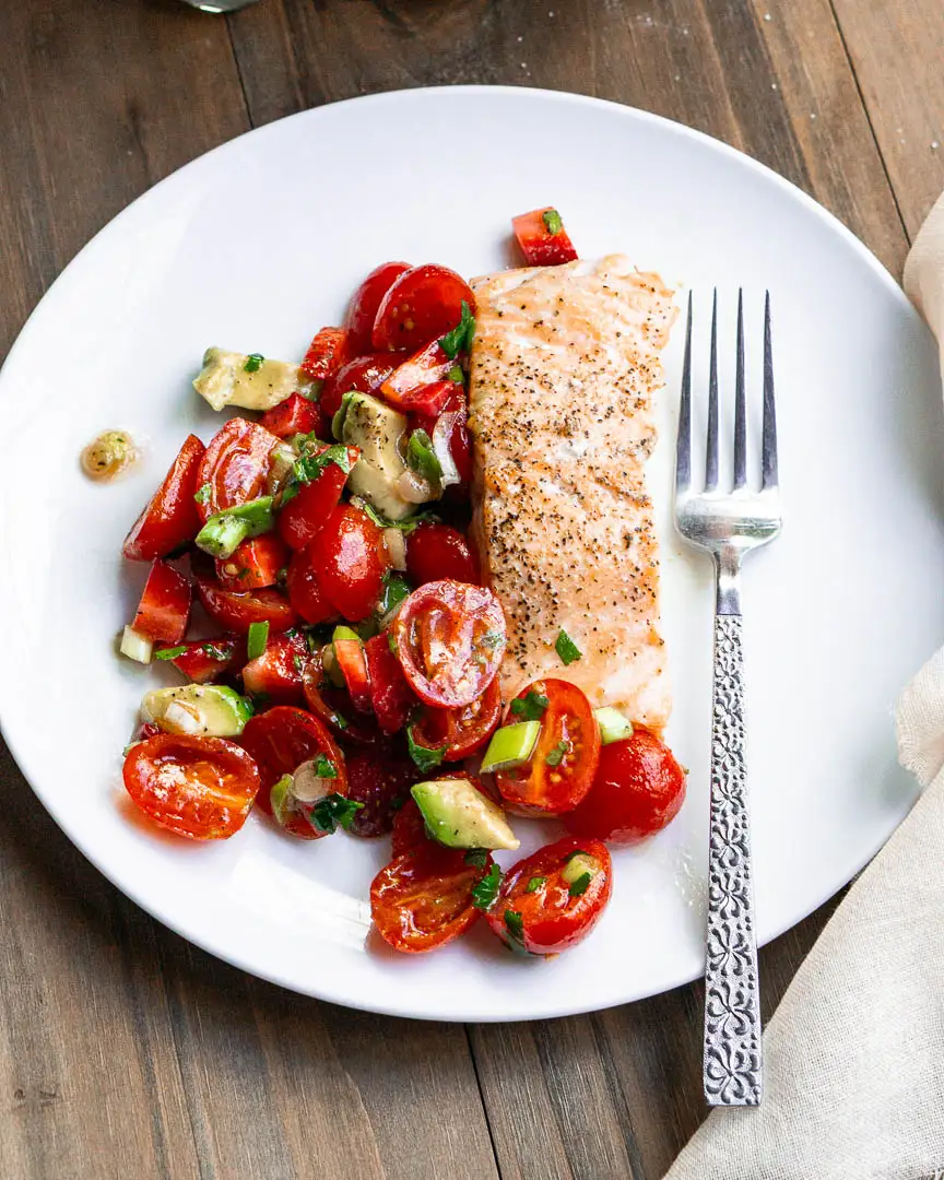 A salmon fillet with Strawberry Salsa on a plate with a fork next to it.