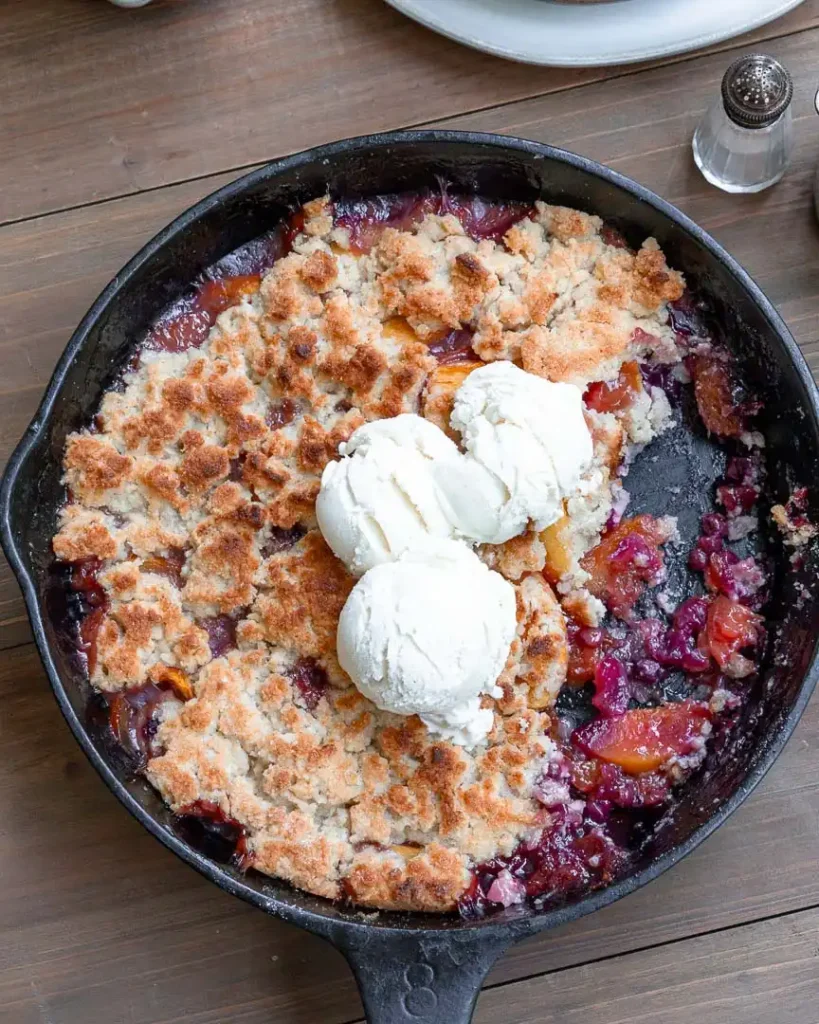Blueberry peach cobbler with a scoop missing and scoops of ice cream on top of it.