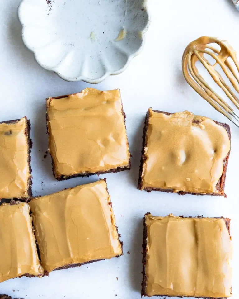 Brownie squares laying next to each other. there is a whisk with frosting sitting next to them.
