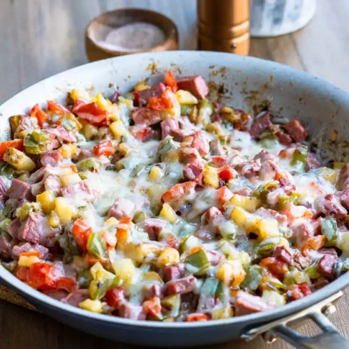 A skillet of corned beef hash with melted cheese on top of it.
