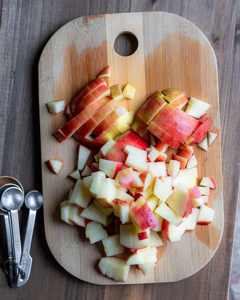 Chopped apples on a cutting board with measuring spoons laying next to them.