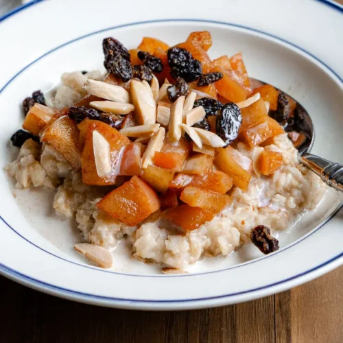 A bowl of oatmeal with toppings like sautéed apples, raisins, slivered almonds.