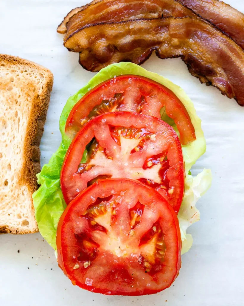 Sliced tomatoes on top of lettuce on a half slice of bread.