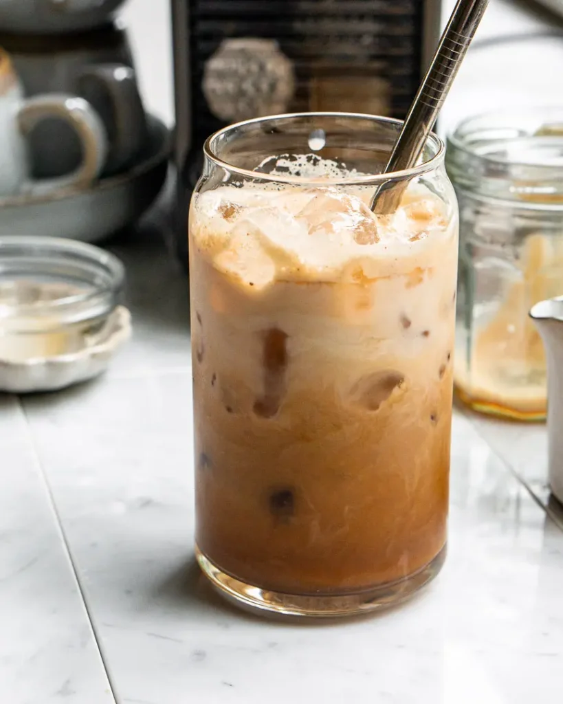 A tall glass with an iced French Toast latte with a metal straw sticking out of it.