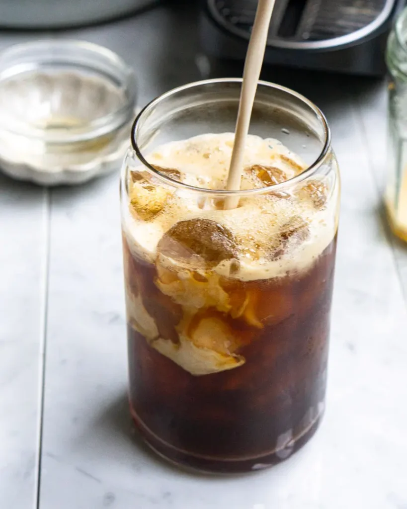 Milk being poured into a tall glass of iced coffee.