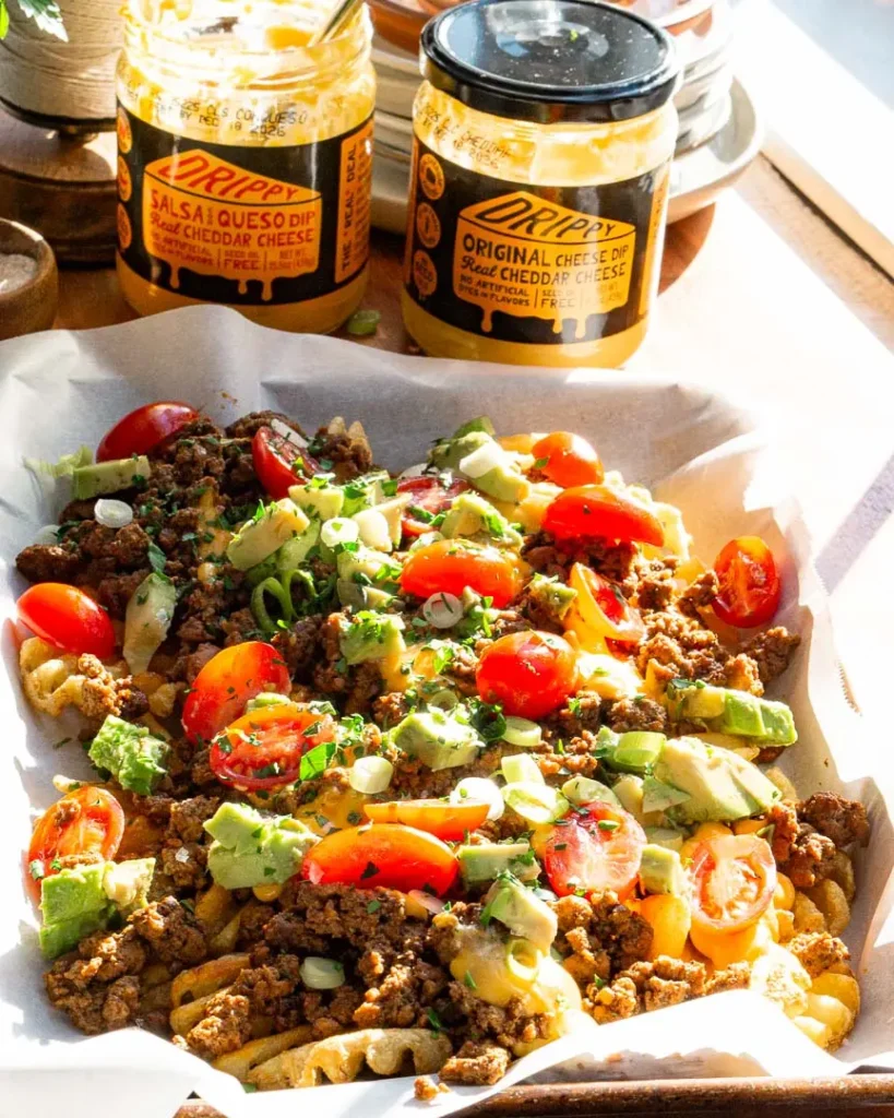 A tray of loaded waffle fries with two jars of cheese sauce behind it.