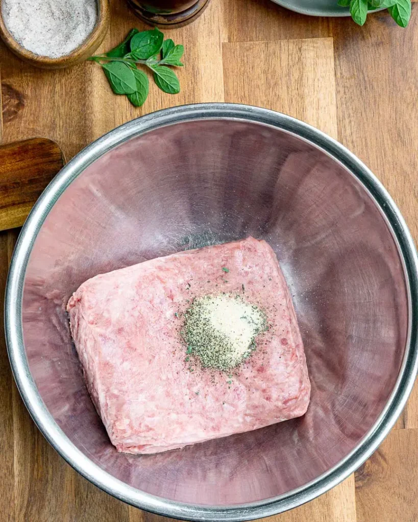 Ground lamb in a bowl with seasoning on top of it ready to be mixed in.