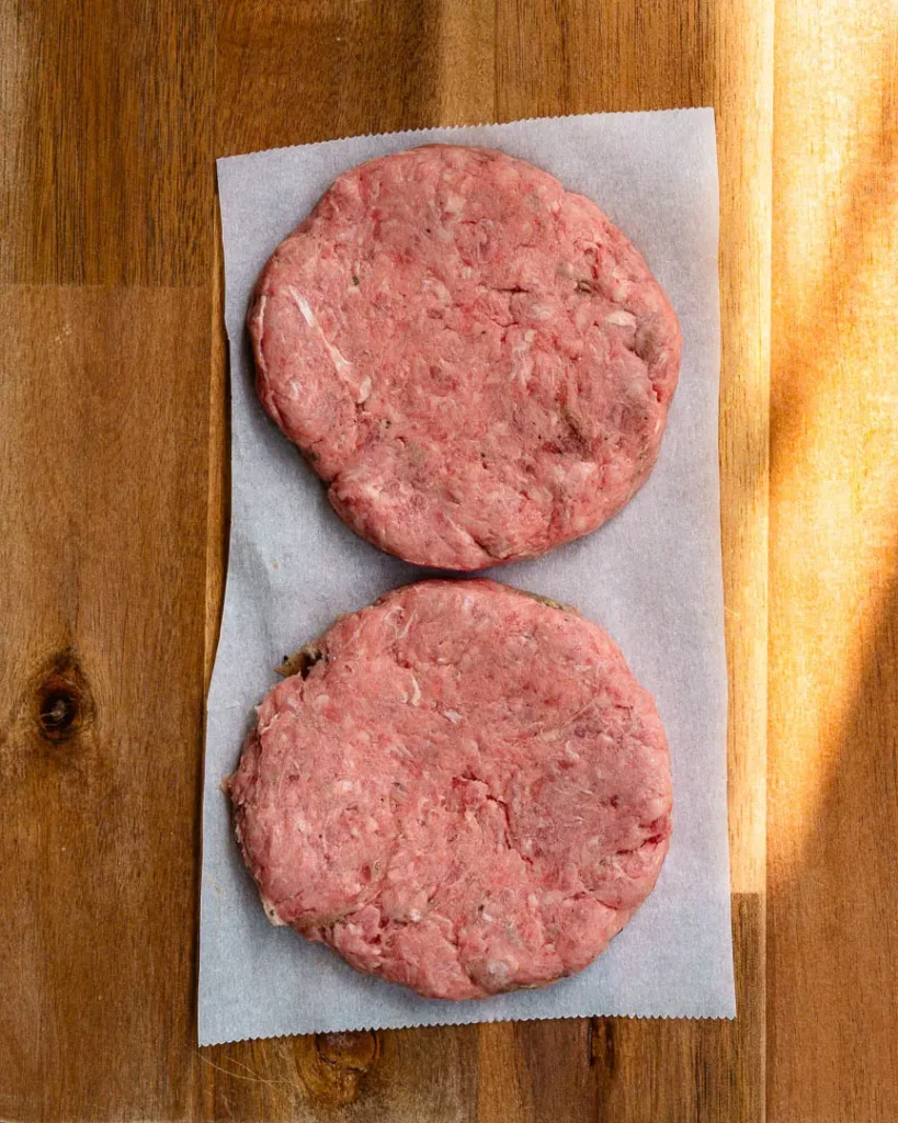Two lamb burger patties on parchment paper waiting to be grilled.