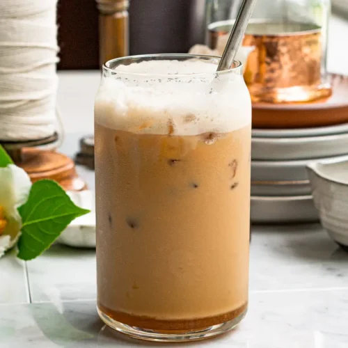 A tall glass of iced salted honey latte with a metal straw sticking out of it.