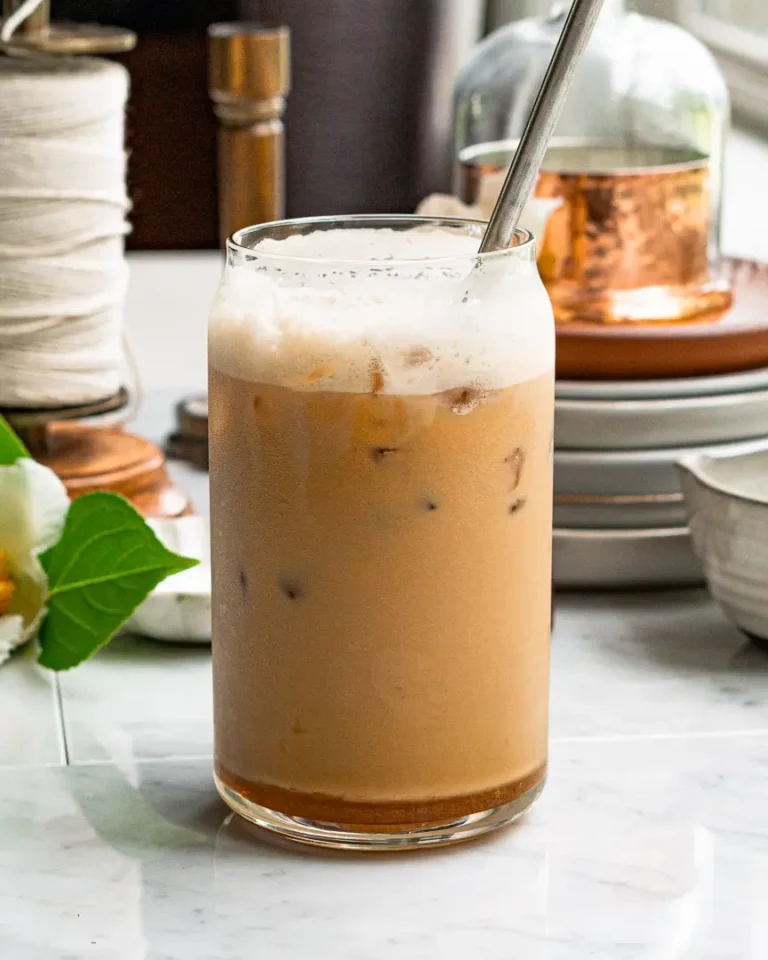 A tall glass of iced salted honey latte with a metal straw sticking out of it.