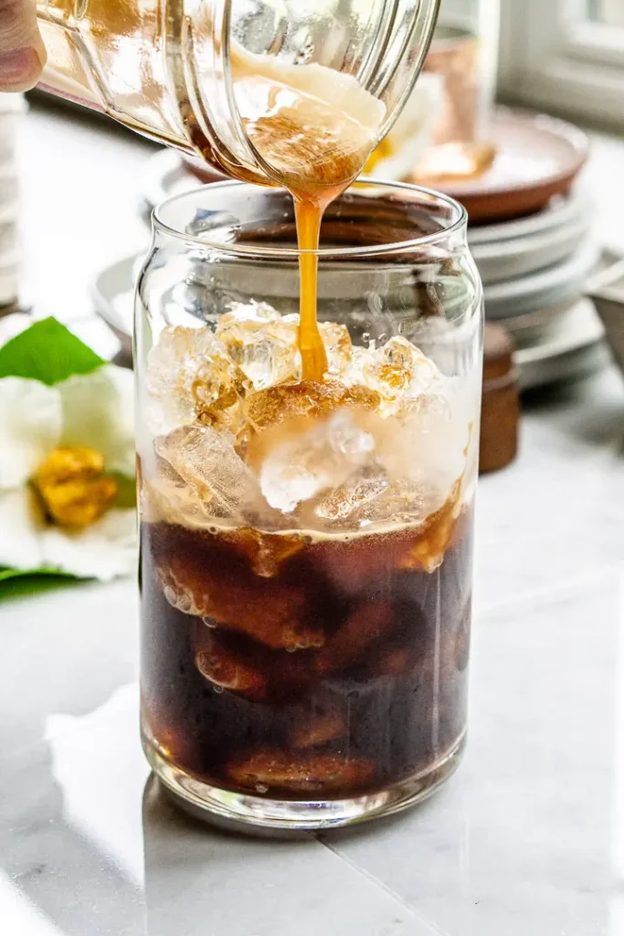 A tall glass with ice in it. There is coffee being poured over the ice.