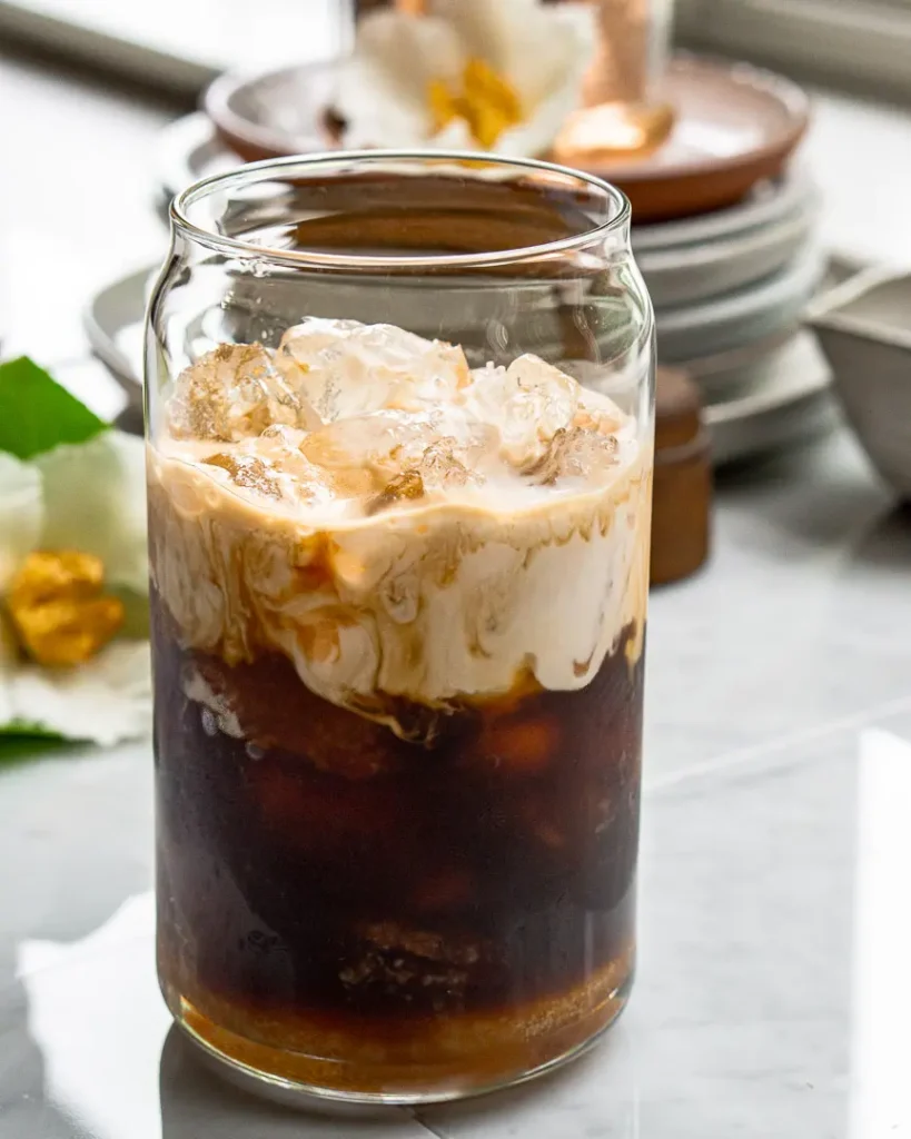 A tall glass of ice with a double shot of expresso with milk sitting on top of the expresso.