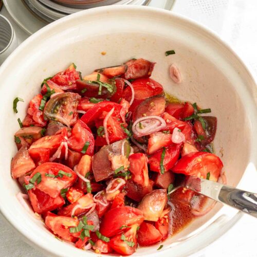 A simple tomato salad in a bowl with a serving spoon.