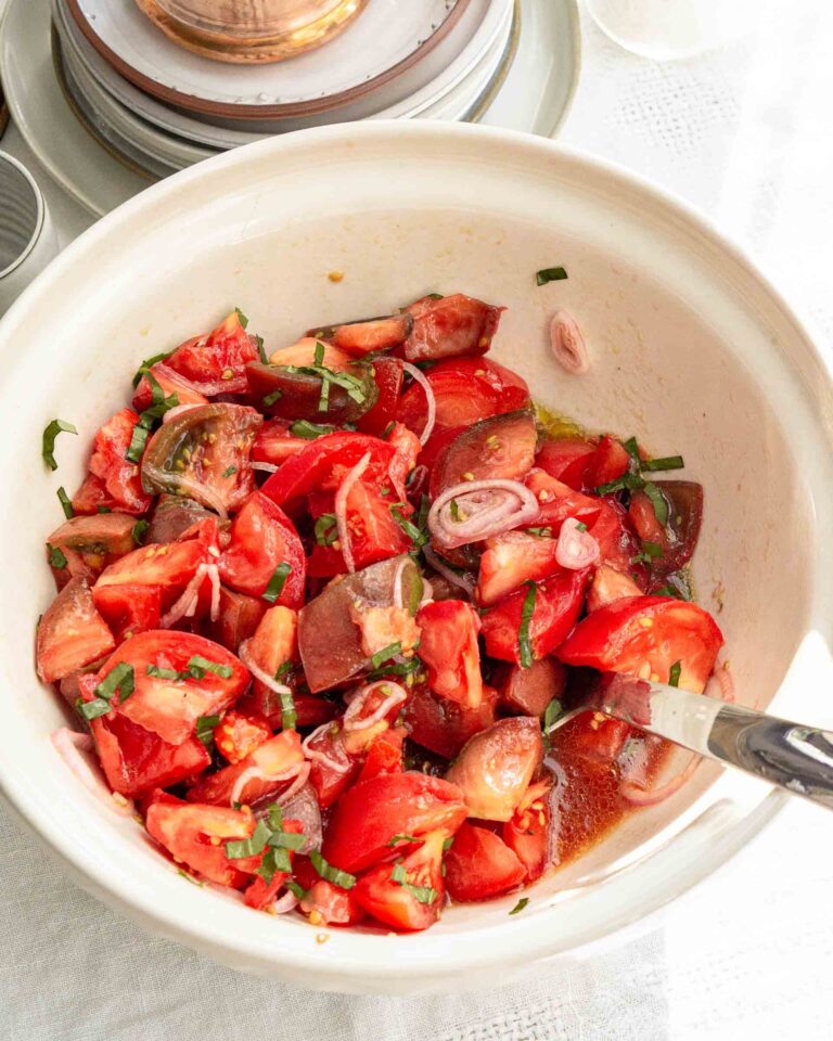 A simple tomato salad in a bowl with a serving spoon.