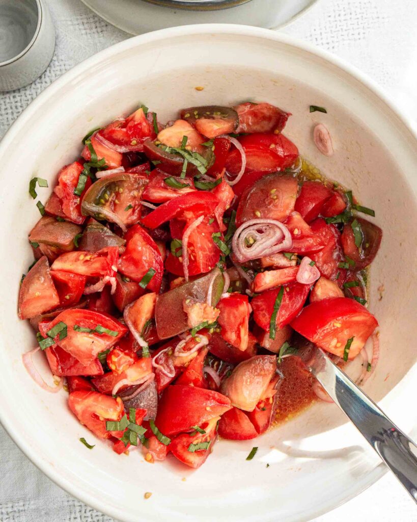 Large tomatoes in a bowl with shallots and fresh basil.