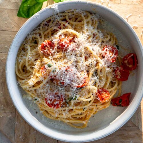 A bowl of spaghetti with cherry tomatoes. The pasta is sprinkled with grated parmesan cheese.