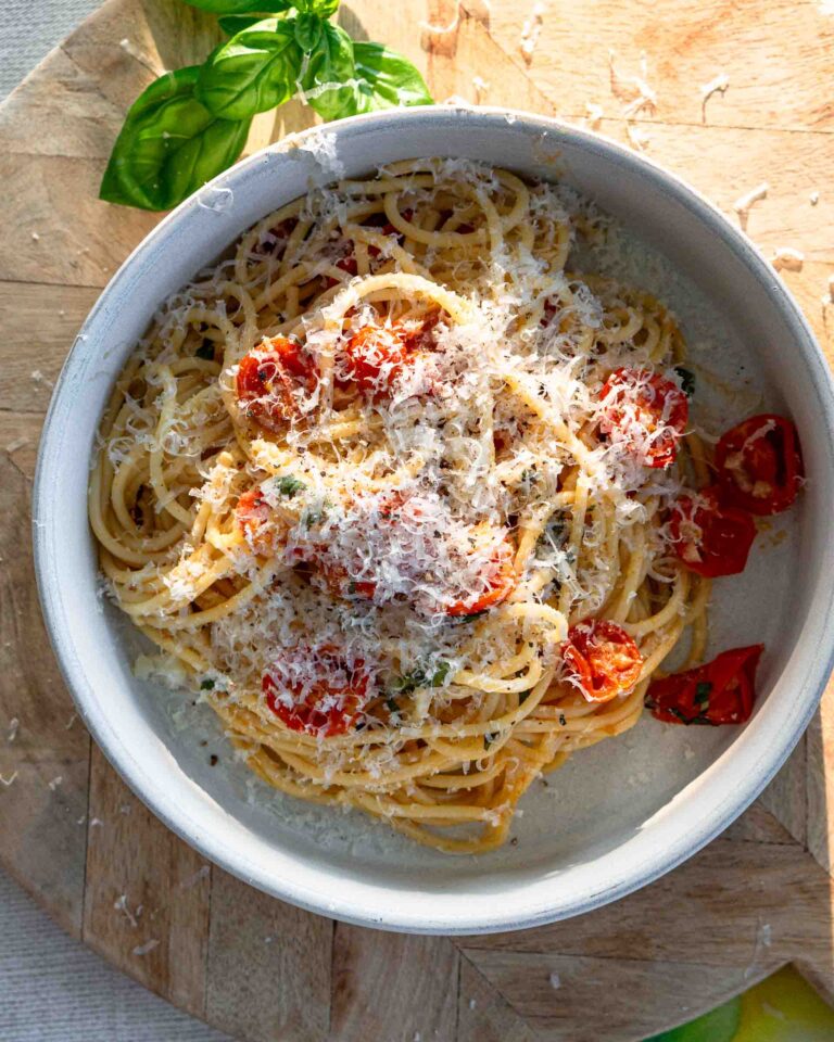 A bowl of spaghetti with cherry tomatoes. The pasta is sprinkled with grated parmesan cheese.