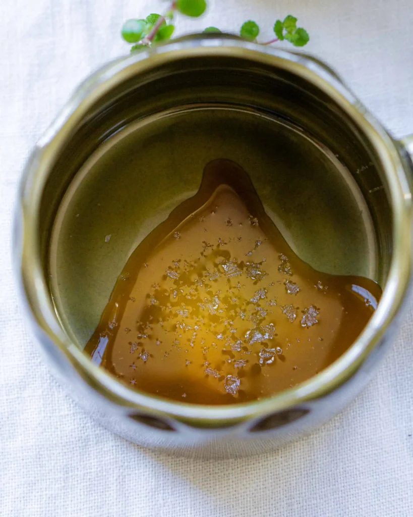 The interior of a mug that has honey and sea salt flakes at the bottom of it.
