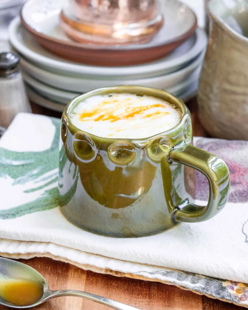 A mug of hot salted honey latte with a caramel drizzle. The mug is sitting on a dish towel.