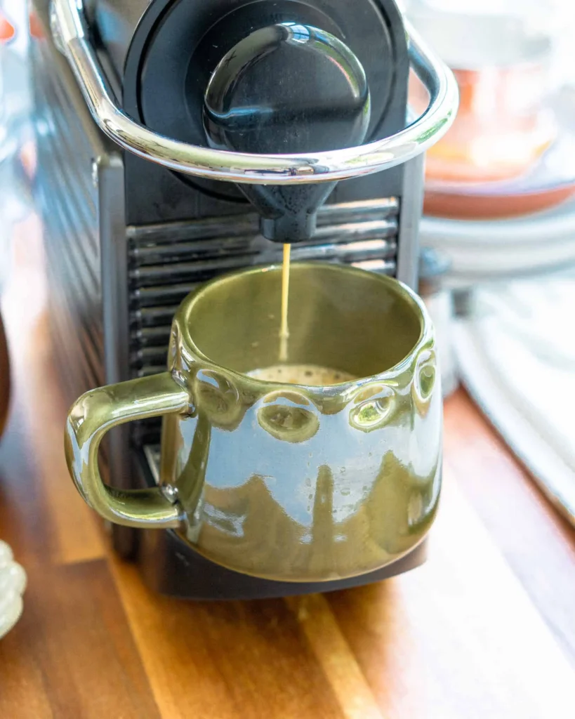 A mug placed in an Nespresso machine. There is espresso coming out of the machine and into the mug.